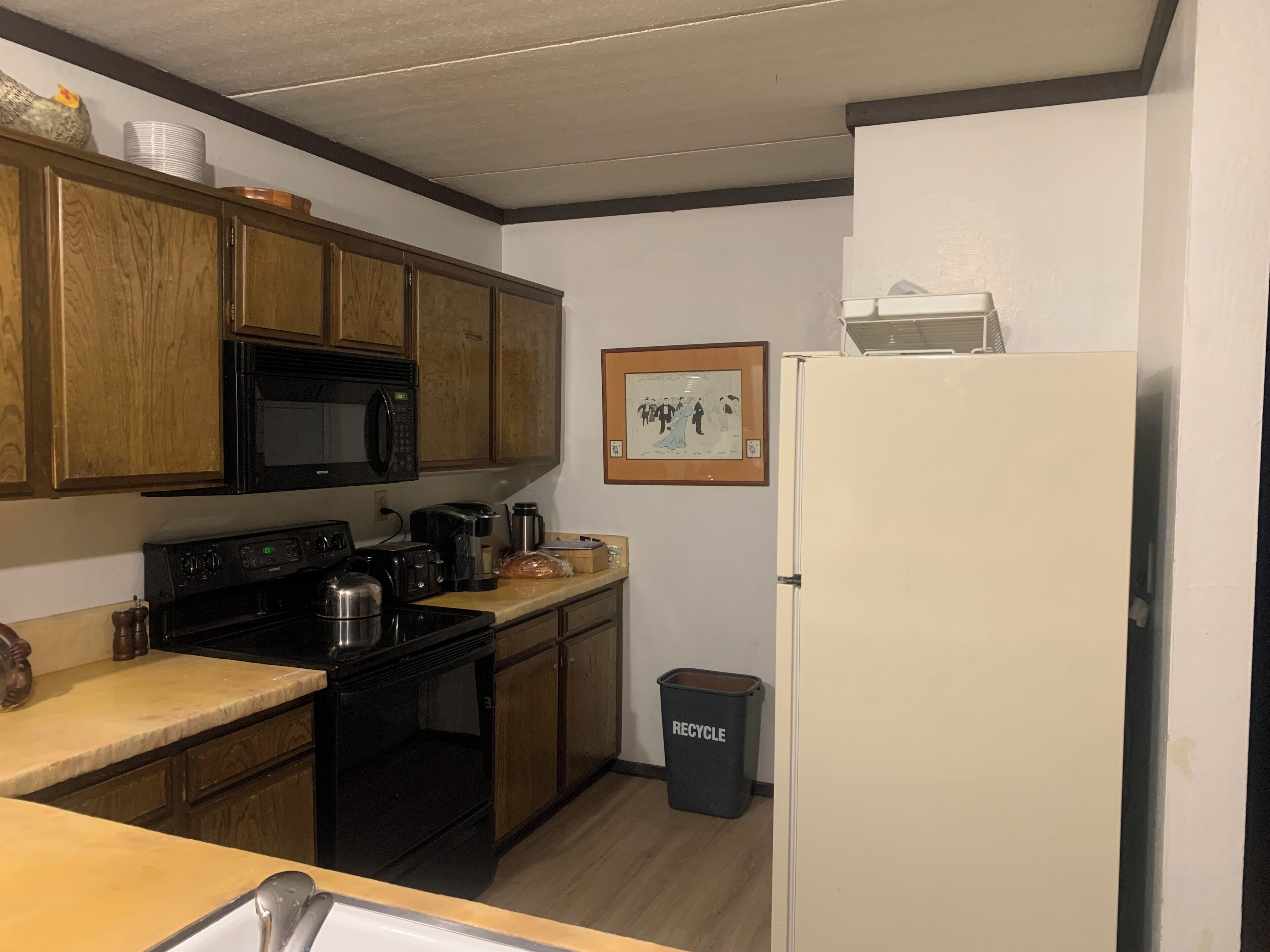 A compact kitchen with wooden cabinets, a microwave, a stove, and a white refrigerator.