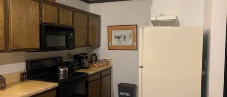 A compact kitchen with wooden cabinets, a microwave, a stove, and a white refrigerator.