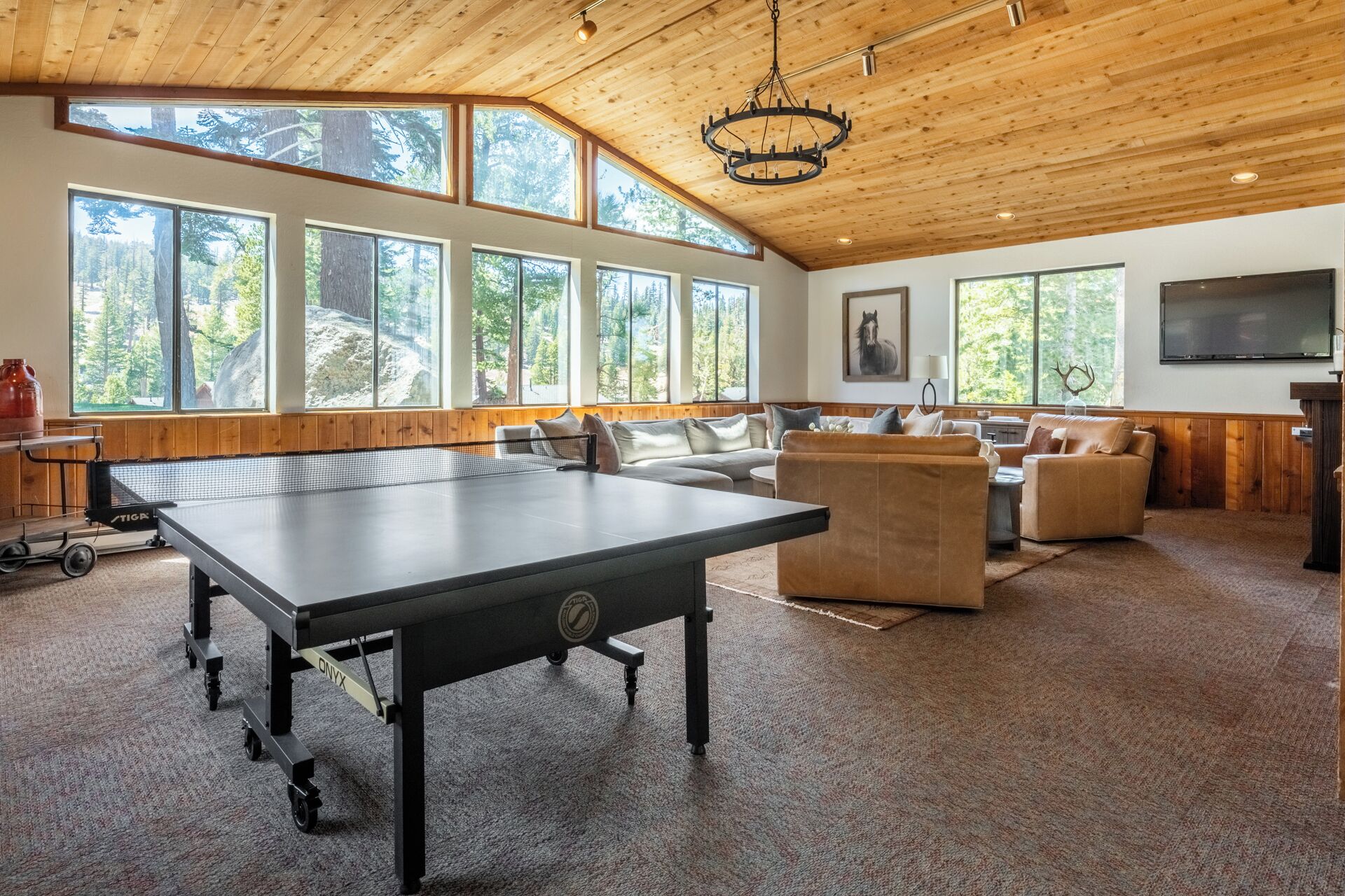 A spacious room with a ping pong table, multiple seating areas, large windows, and a wooden ceiling.