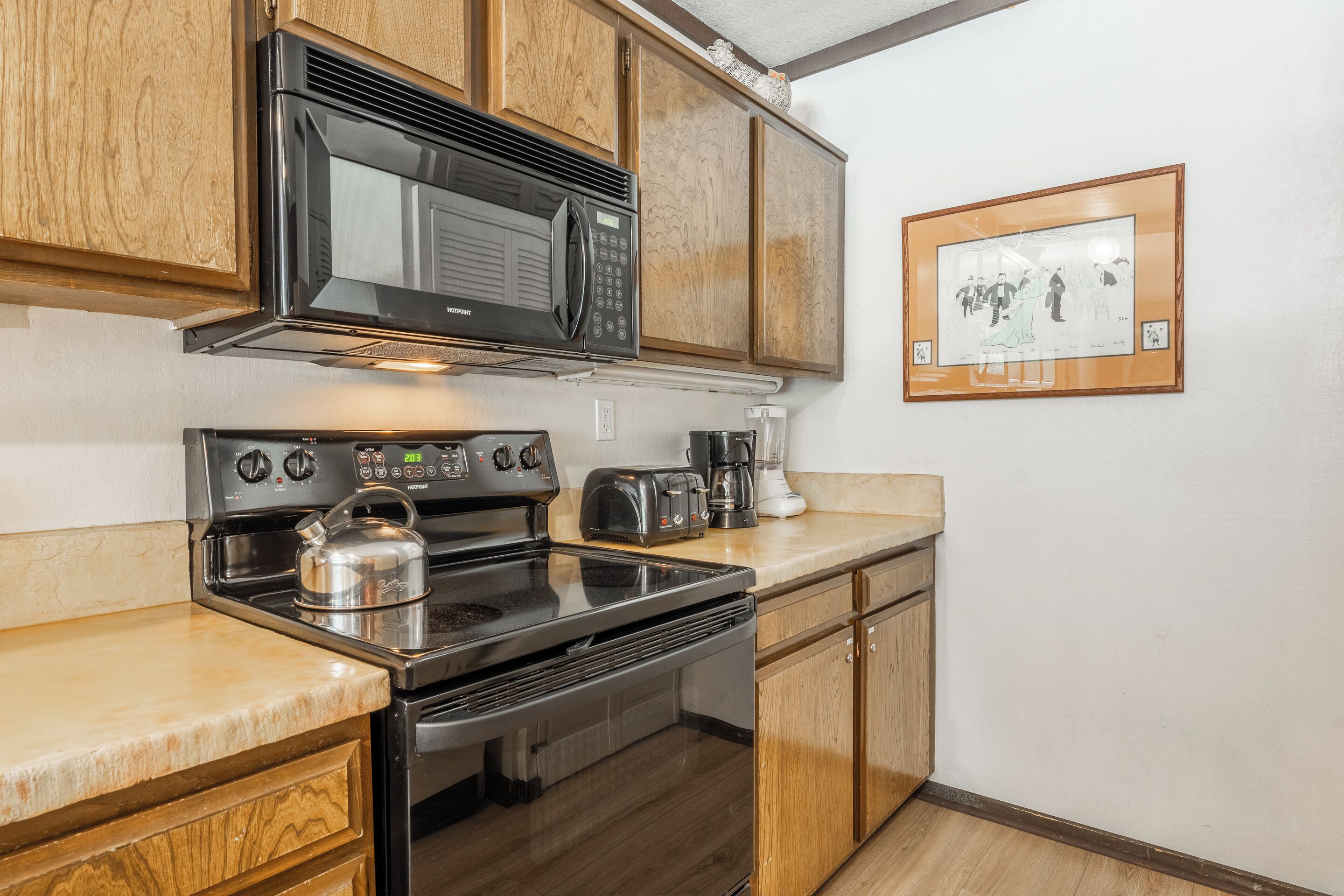 Una cocina compacta con armarios de madera, estufa de acero inoxidable, microondas, tostadora y cafetera.