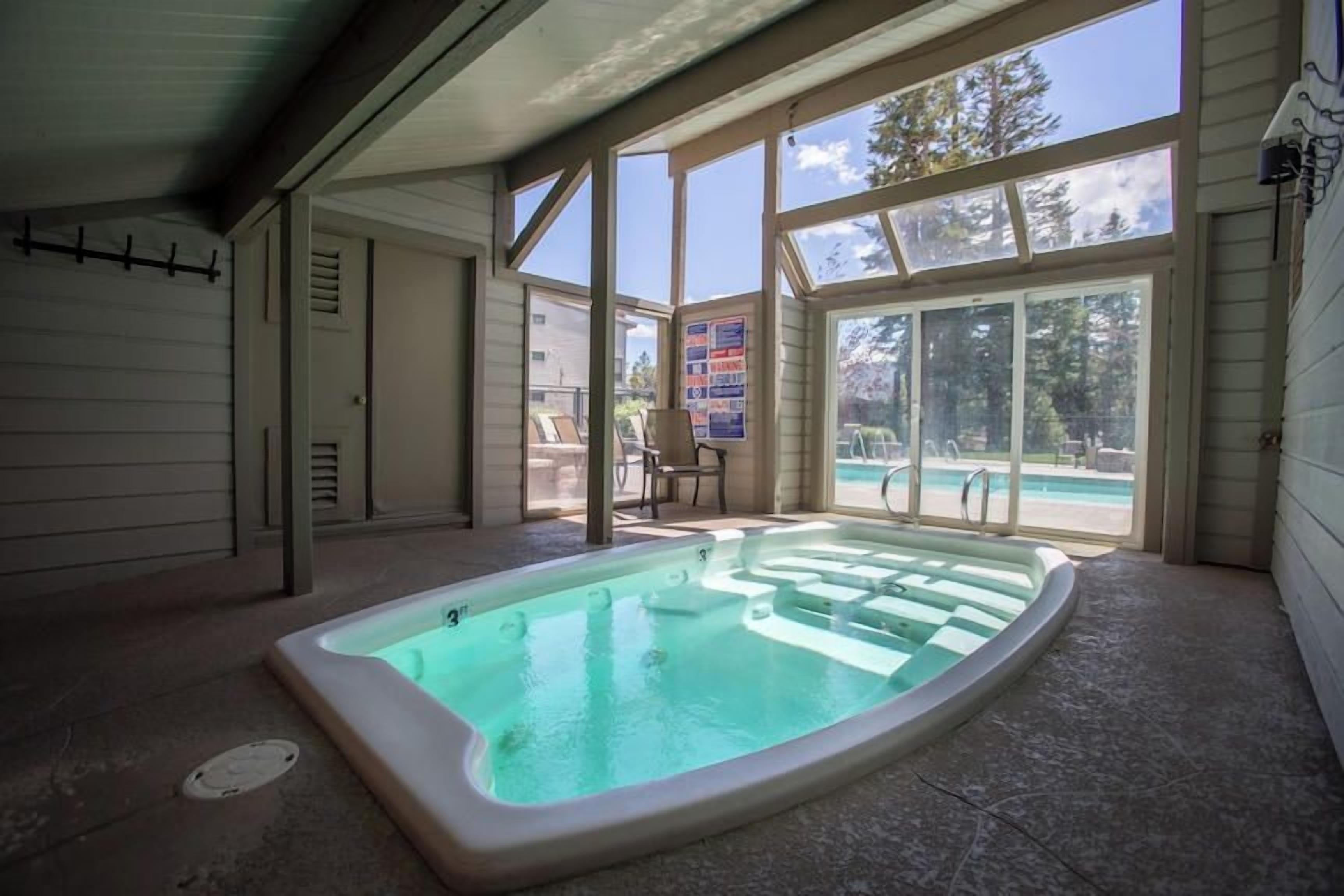 Un bain à remous situé dans un espace extérieur abrité, avec vue sur une piscine et des arbres.