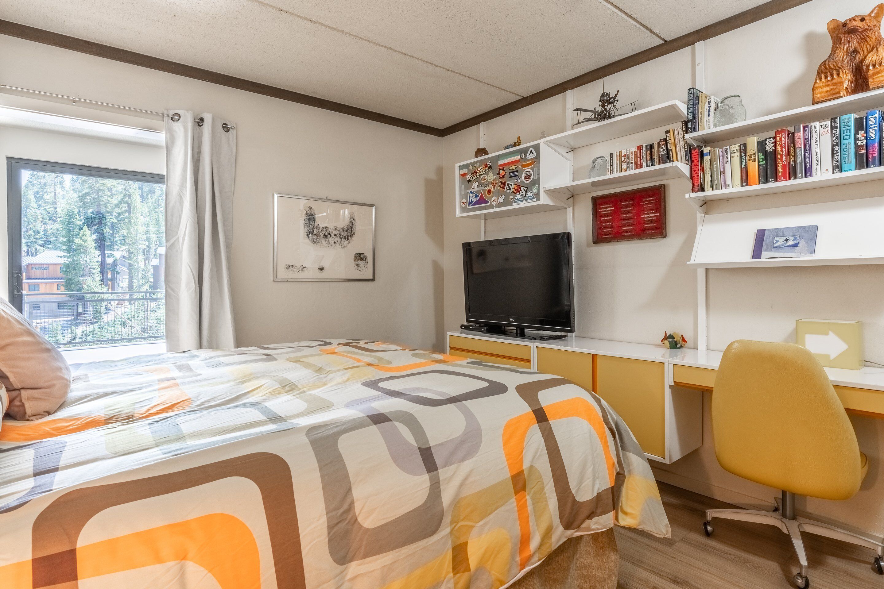 Een slaapkamer met een bed, een bureau met een computer, een stoel, een televisie en boekenkasten.