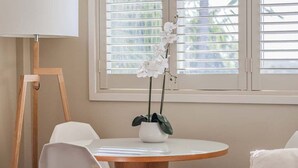A round wooden table with a white vase containing white flowers, a white chair, and a white lamp. - The Pool Resort Kingscliff - 1BR with Hinterland Views (5312) - Holiday Management Co. (Tweed)