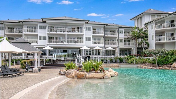 A multi-story hotel with balconies, a pool area with lounge chairs, and a covered patio. - The Pool Resort Kingscliff - 1BR with Hinterland Views (5312) - Holiday Management Co. (Tweed)