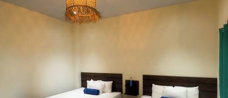 Een hotelkamer met twee bedden, elk met een wit- en blauwe spreidek, een houten hoofdbord en een hangende lamp.