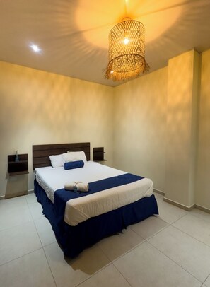 A neatly made bed with a white and blue bedspread, two nightstands with lamps, and a textured ceiling light fixture.