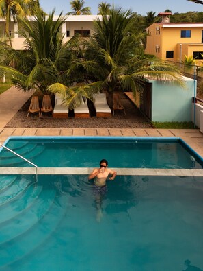 A swimming pool with a person in it, surrounded by palm trees and lounge chairs.