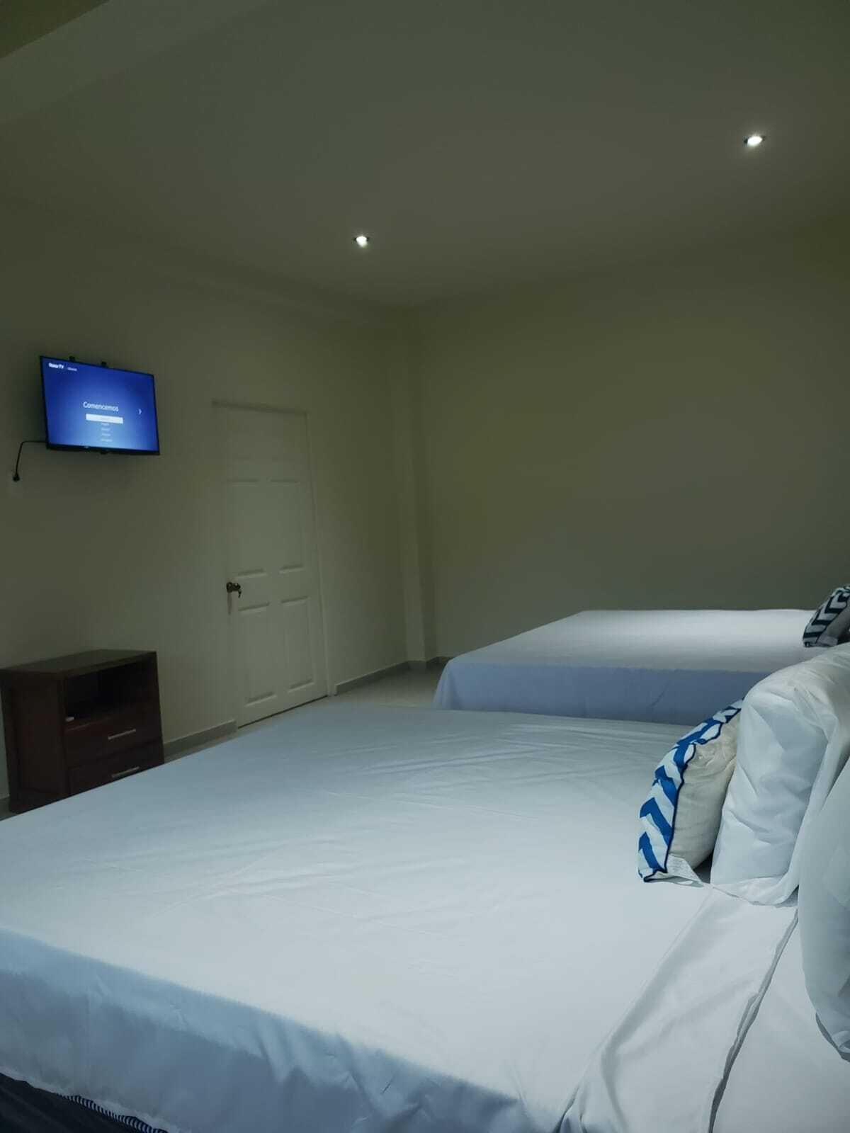 Un dormitorio con dos camas, un televisor en la pared y un mueble pequeño.