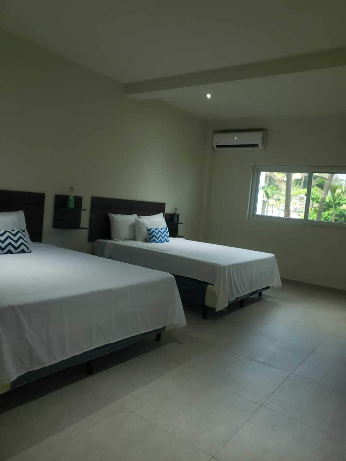 Une chambre d’hôtel avec deux lits simples, une fenêtre donnant sur un espace verdoyant et un climatiseur fixé au mur.