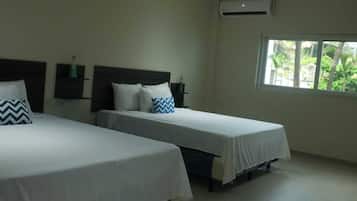 Une chambre d’hôtel avec deux lits simples, une fenêtre donnant sur un espace verdoyant et un climatiseur fixé au mur.