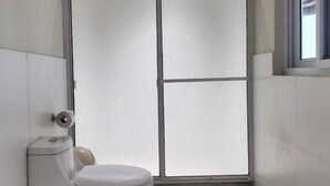 Un baño pequeño y funcional con inodoro, cabina de ducha y ventana.