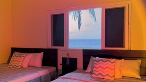 Habitación de hotel con dos camas, una ventana con vista al océano y una mesita de noche con lámpara.