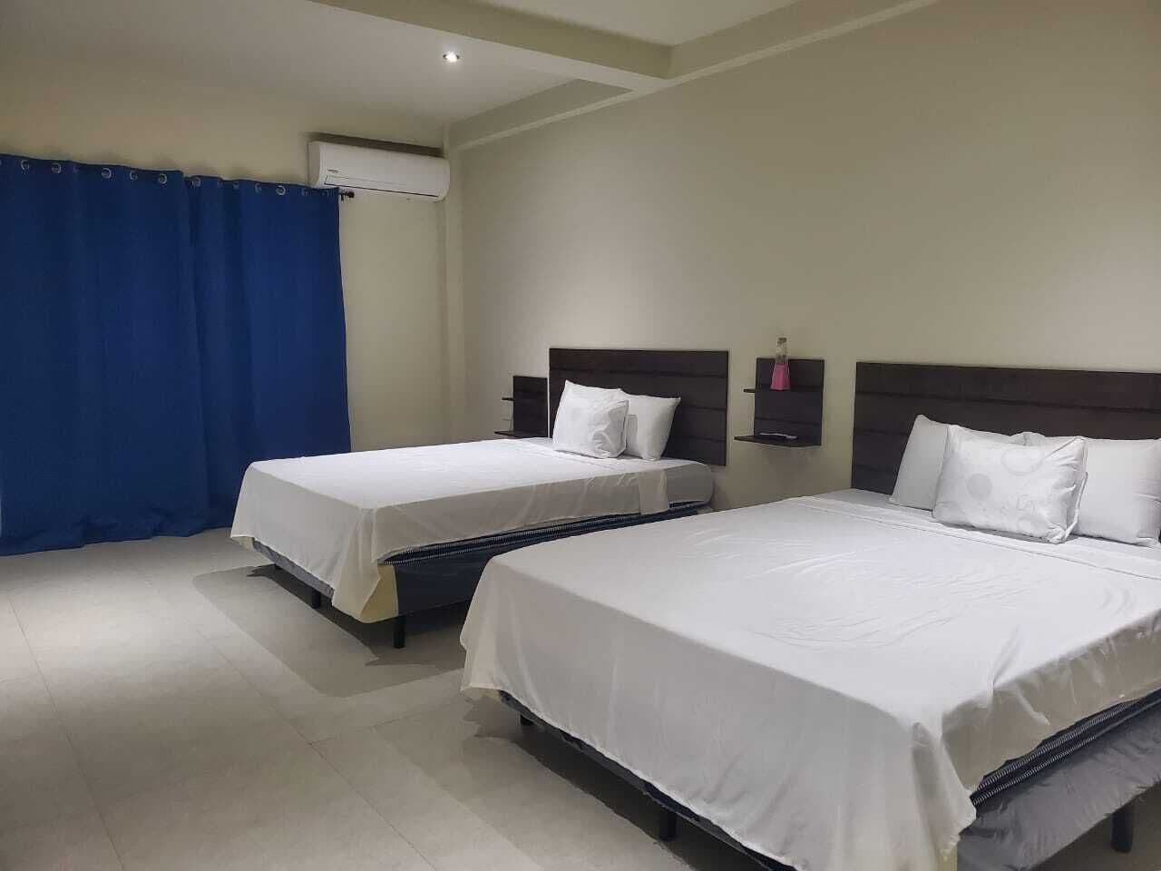 A hotel room with two single beds, a blue curtain, and a wall-mounted air conditioner.