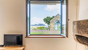 A room with a large window overlooking a garden and a stone building. - La petite Pen Er Hoët by Interhome (La Trinité Sur Mer)
