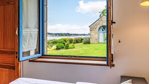 A bedroom with a large window offering a view of a stone building and a grassy area. - La petite Pen Er Hoët by Interhome (La Trinité Sur Mer)
