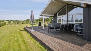Una terraza techada al aire libre con mesa y sillas, una parrilla y vistas del paisaje circundante.