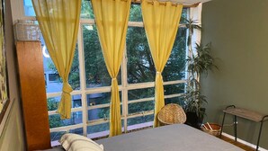 Une chambre à coucher avec un lit, une fenêtre avec des rideaux jaunes, une plante en pot et une petite table.