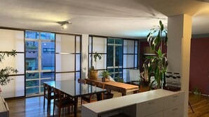 Un vaste espace dédié à la salle à manger, avec une table et des chaises en bois, de grandes fenêtres et des plantes en pot.