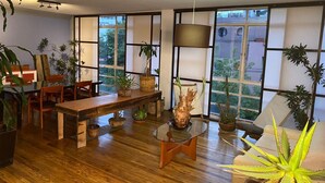 Un salon spacieux doté d’un plancher en bois, d’une table à manger, de chaises, d’une table basse en verre et de diverses plantes en pot.