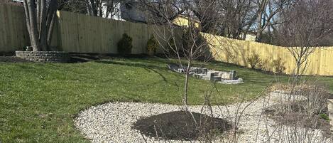 A landscaped backyard with a gravel path, a small tree, and a yellow fence.