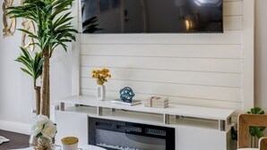 Un salon moderne avec un téléviseur à écran plat fixé à un mur blanc, une table basse ronde agrémentée d’objets décoratifs et des sièges confortables.
