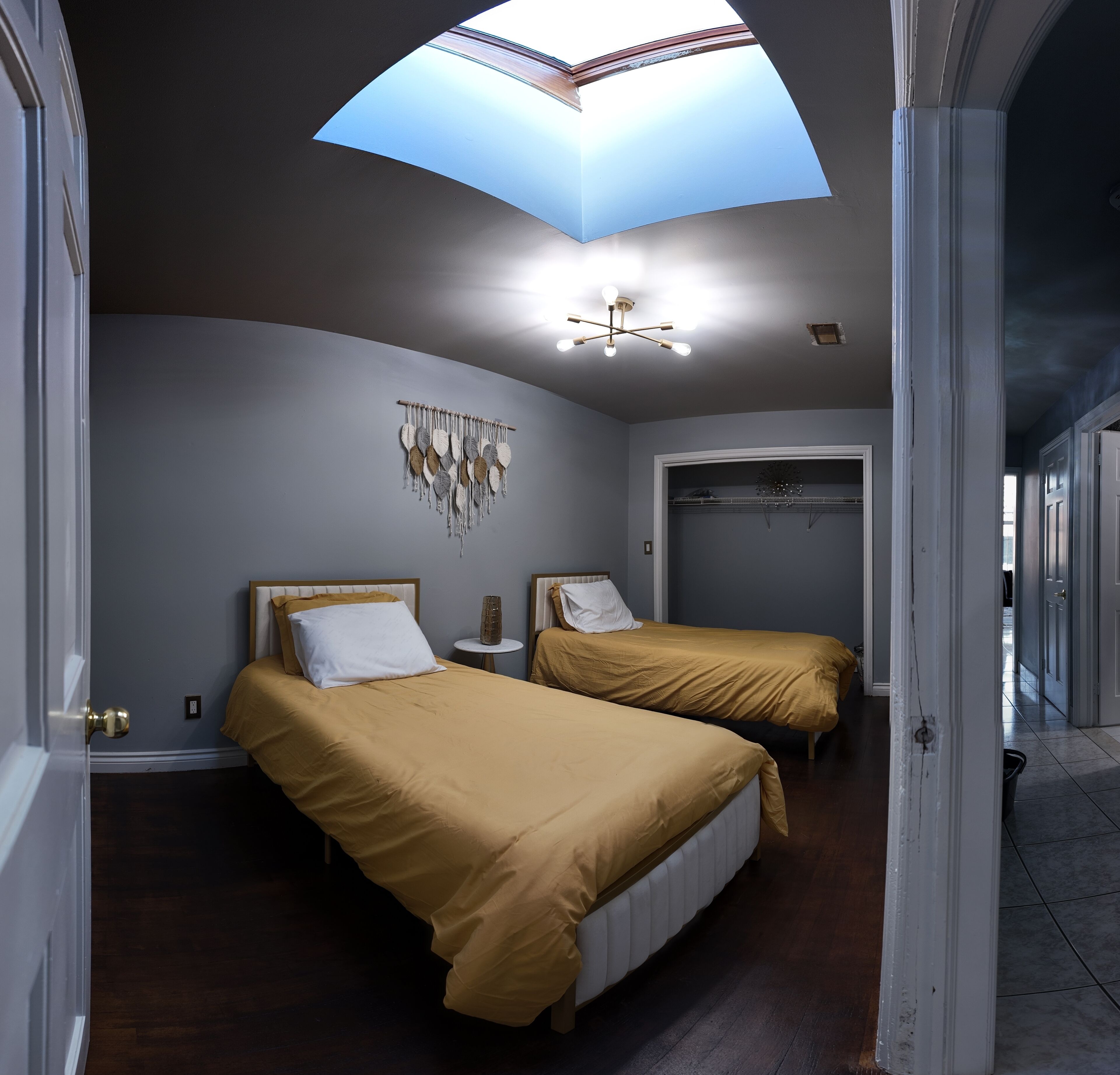 A bedroom with two beds, a skylight, a chandelier, and a wall-mounted decor piece.