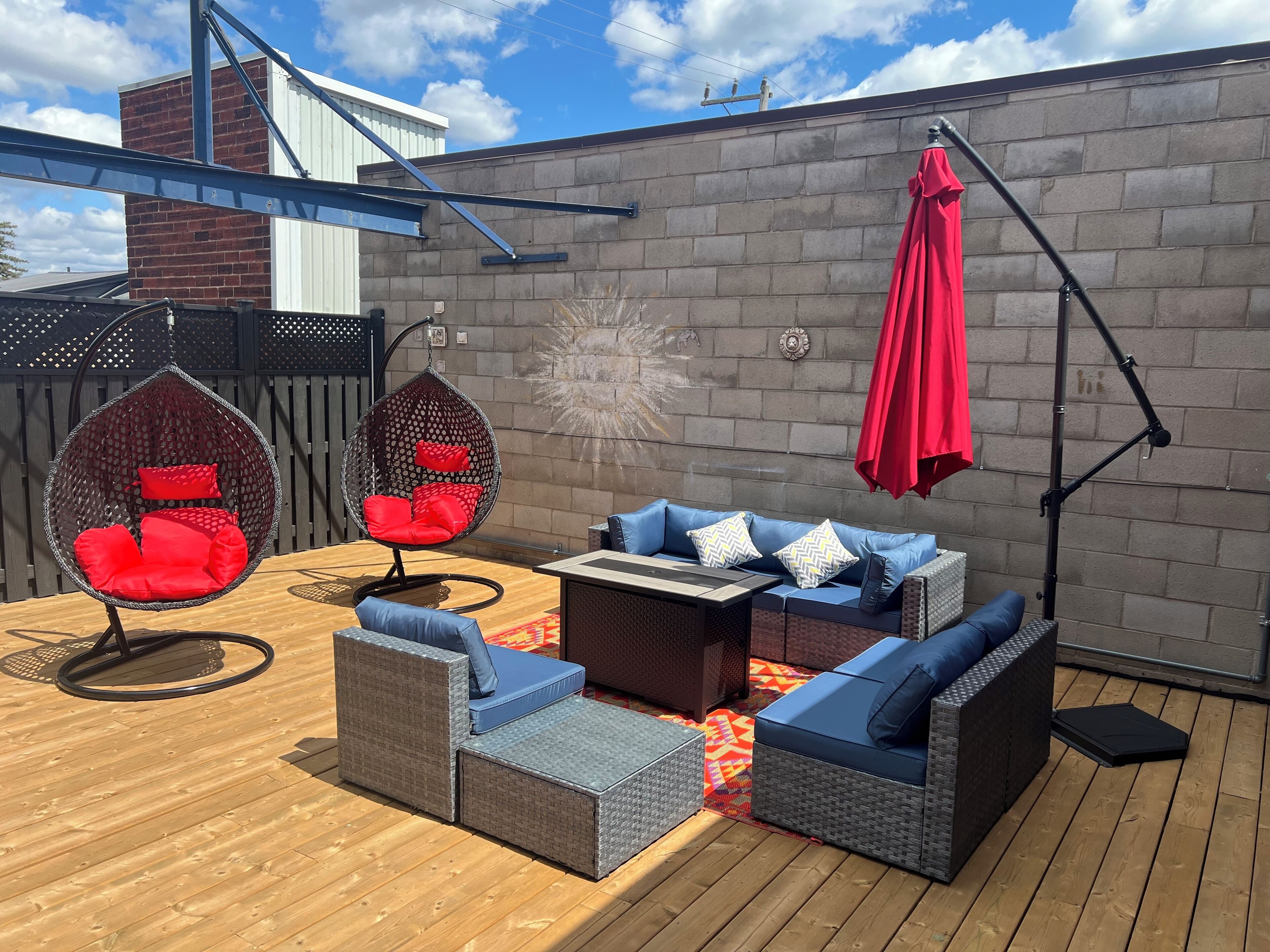Une terrasse dotée de meubles en osier, d’un fauteuil suspendu et d’un parasol rouge.
