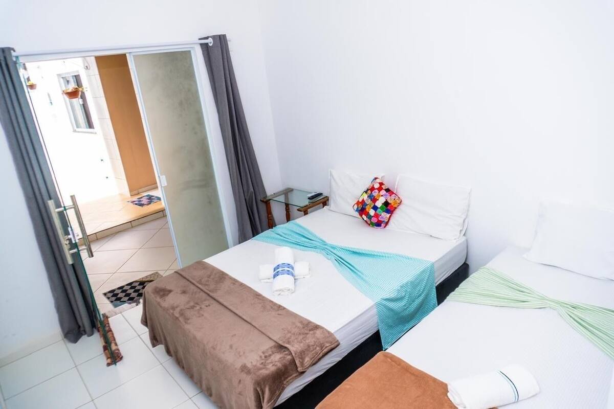 Ein Hotelzimmer mit Bett, kleinem Tisch, Stuhl und einem Fenster mit Vorhängen.
