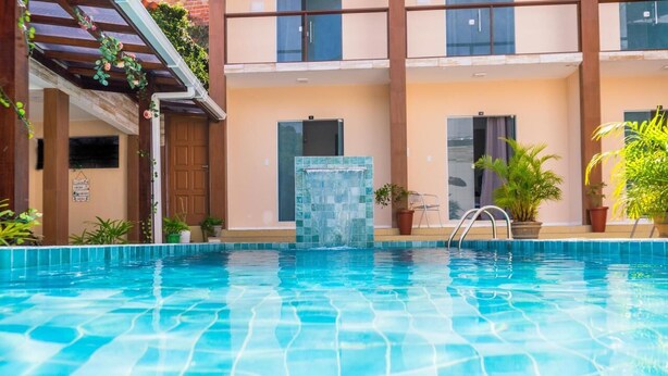 A swimming pool with a tiled edge, a glass door, and potted plants around the pool area. - Pousada Cairu  (Cairu)
