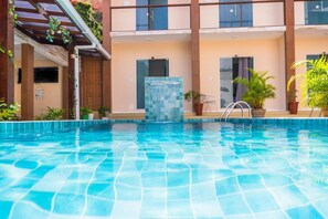 Une piscine dont le bord est recouvert de carrelage, une porte en verre et des plantes en pot disposées autour de la piscine.