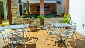 An outdoor patio area with metal tables and chairs, a wooden bench, and potted plants. - Pousada Cairu  (Cairu)