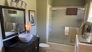 Un baño con un espejo grande, un lavamanos blanco, un inodoro y una ducha con mampara de vidrio.