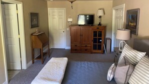 Un dormitorio con una cama, un televisor sobre un mueble de madera, un ventilador de techo y una puerta.