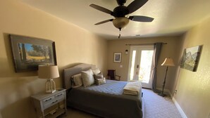 Un dormitorio con cama, mesita de noche, ventilador de techo, puerta con vistas y lámpara.