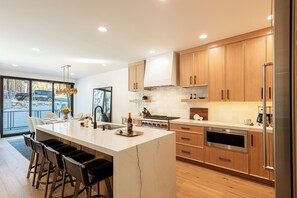 A modern kitchen with a large island, wooden cabinets, and stainless steel appliances.