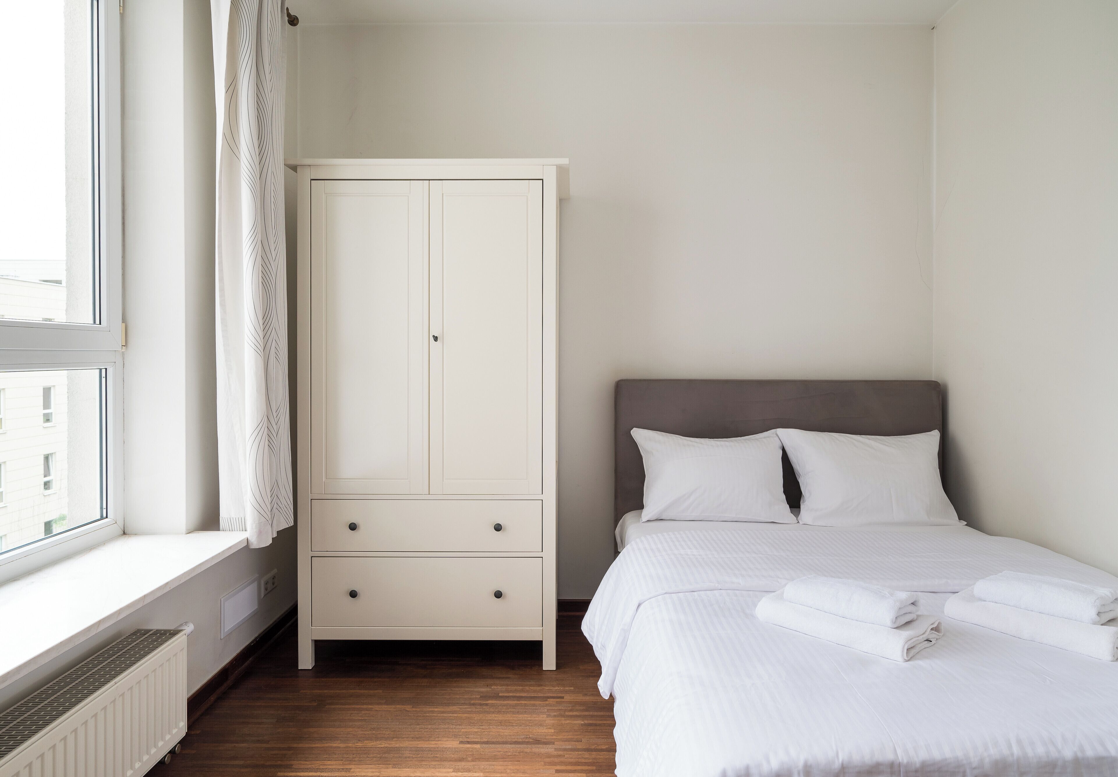 A bedroom with a bed, a wardrobe, and a window with curtains.