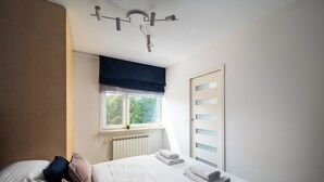 Een slaapkamer met een bed, kussens, een raam met uitzicht, een radiator en een deur.