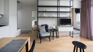 Un salon moderne avec un plancher en bois, un canapé gris, un fauteuil noir, une petite table ronde et un bureau blanc avec un ordinateur.