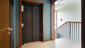 A hallway with a dark door, a wooden door frame, and a tiled floor leading to a staircase with a wooden railing.