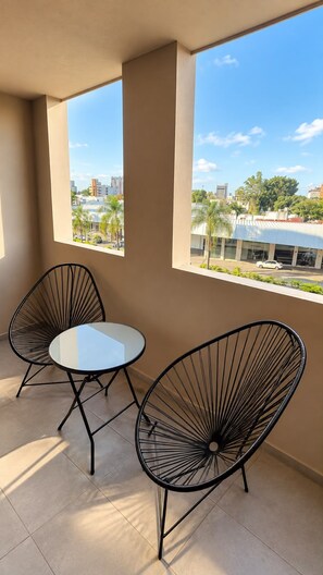 A balcony with two black wire-framed chairs and a small round table.