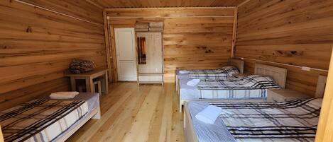 A wooden cabin room with three beds, a small table, and a door leading to another room.