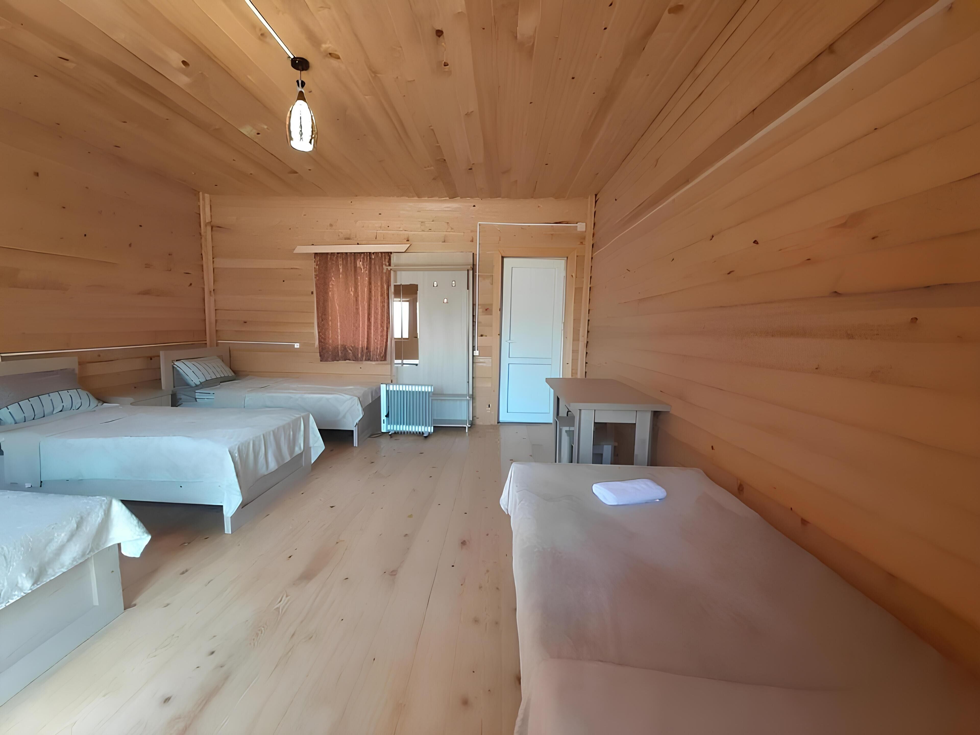 Una habitación de cabaña de madera con dos camas, una mesa, un radiador y una puerta.