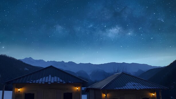 Two wooden cabins with metal roofs, each with a small window and a light fixture, set against a backdrop of snow-covered mountains under a starry night sky. - Ushba Gate House (Mestia)