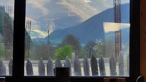 A view of a snow-capped mountain through a window, with a wooden table and chairs inside a room. - Ushba Gate House (Mestia)