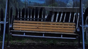 A bench with a metal frame and wooden slats, under a shelter with string lights, set against a backdrop of a snow-capped mountain. - Ushba Gate House (Mestia)