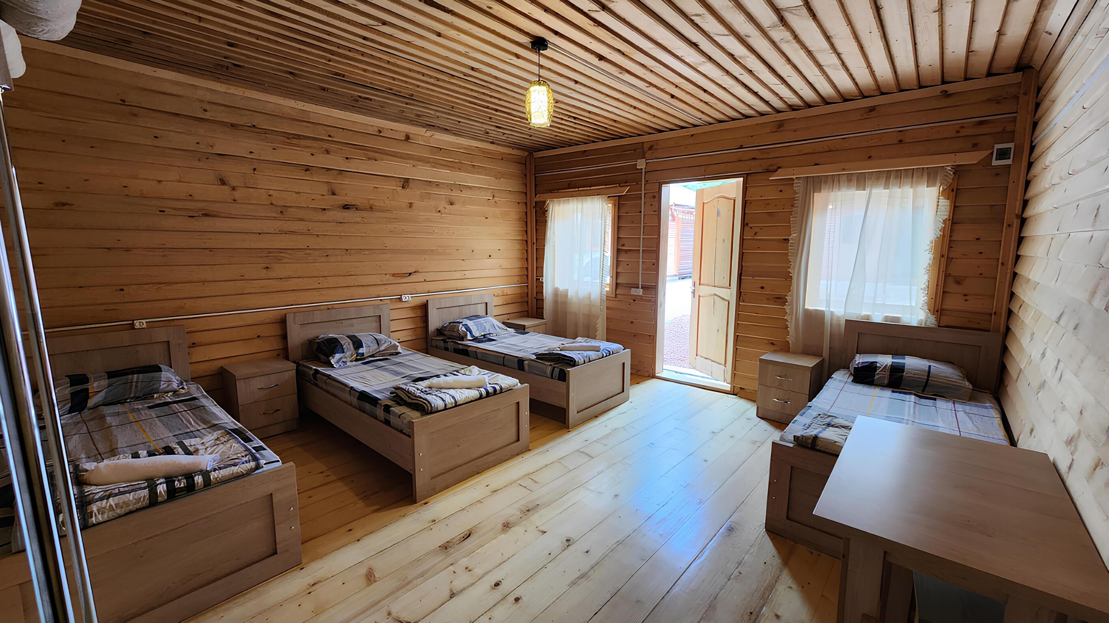 A cabin with three wooden beds, a wooden desk, and a window with curtains.