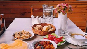 A dining table with various dishes, a pitcher, and a vase with flowers, set against a view of mountains through large windows. - Ushba Gate House (Mestia)