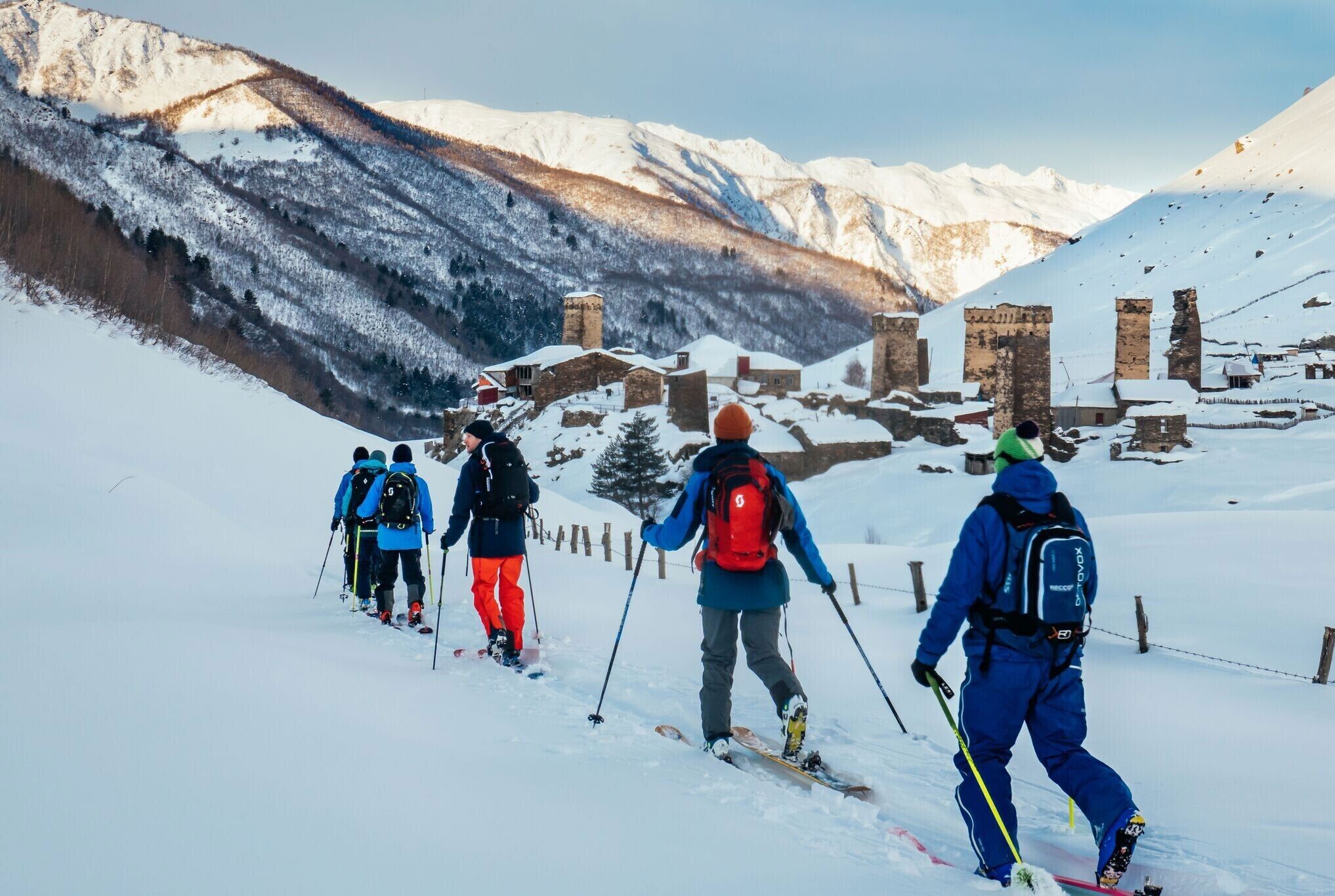 Un grupo de personas esquiando por un sendero nevado en la montaña, con edificios históricos al fondo.