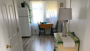 Una habitación con piso de madera, una mesa con sillas, una lámpara y un ventanal con cortinas.