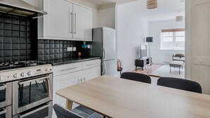 Moderni keittiö, jossa on valkoiset kaapit, mustat laatat välitilassa, kaasuliesi ja jääkaappi. Keittiössä on myös ruokailutila, jossa on puinen pöytä ja tuolit.